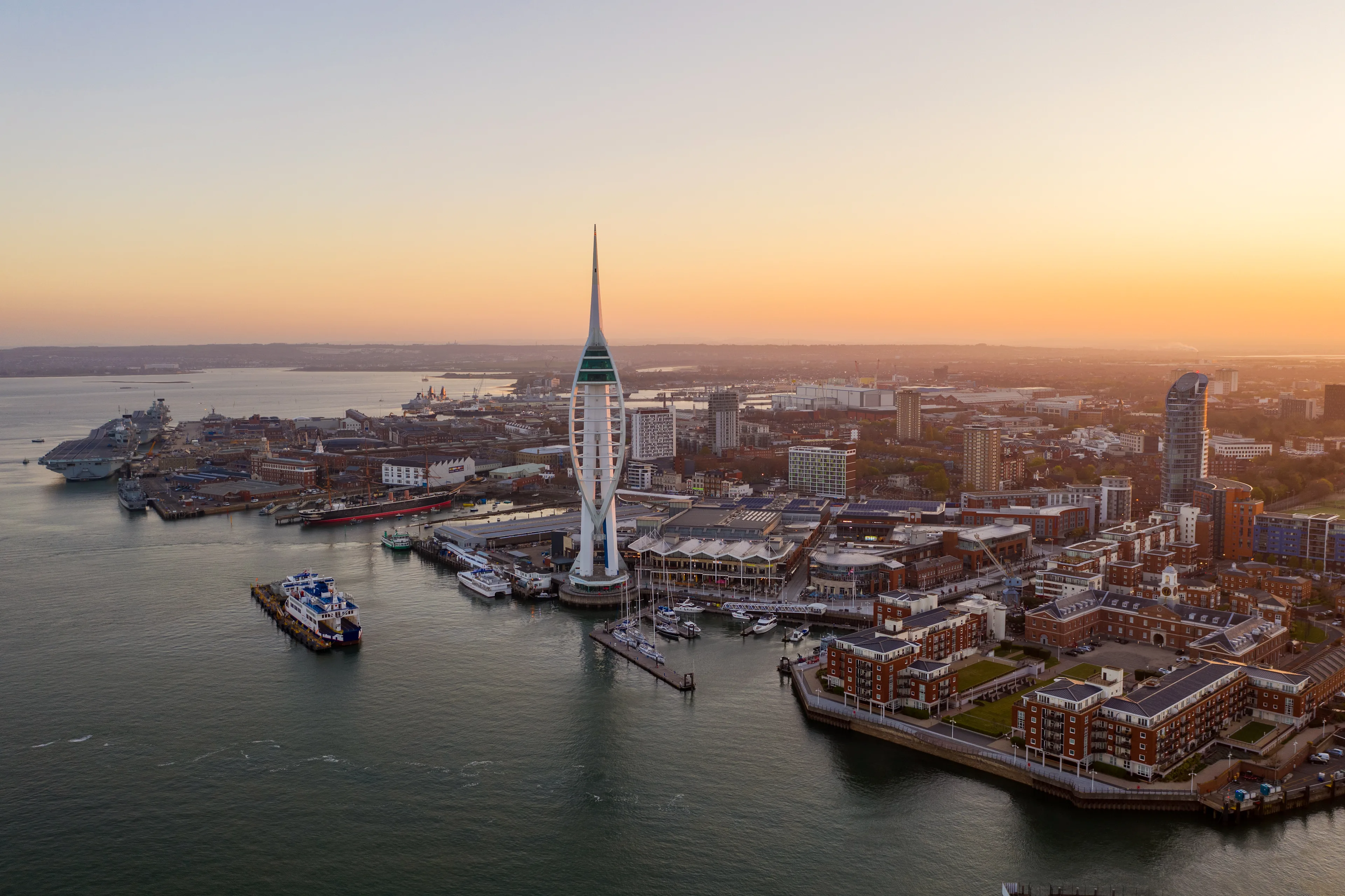 Aerial image at sunset depicting Gunwharf Wharf Quays and the iconic Spinnaker Tower amongst the backdrop of Portsmouth Harbour.
